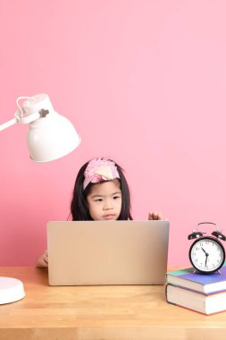 The cute Asian girl learning from internet by laptop with the pink background.
