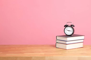 Renk arkaplanlı kitap yığınındaki analog saat ayarı.