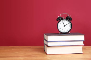 Renk arkaplanlı kitap yığınındaki analog saat ayarı.