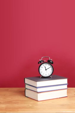Renk arkaplanlı kitap yığınındaki analog saat ayarı.