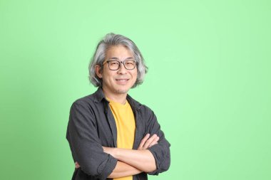 Kıdemli Asyalı, şık giyinmiş açık yeşil arka planda duruyor..