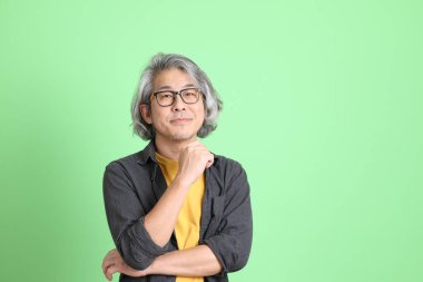 Kıdemli Asyalı, şık giyinmiş açık yeşil arka planda duruyor..