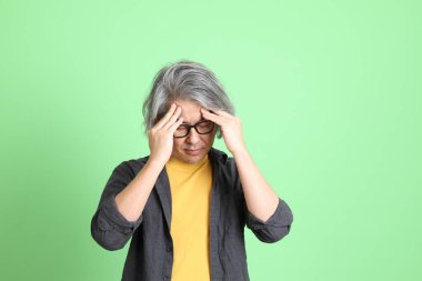 Kıdemli Asyalı, şık giyinmiş açık yeşil arka planda duruyor..