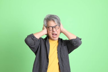 Kıdemli Asyalı, şık giyinmiş açık yeşil arka planda duruyor..