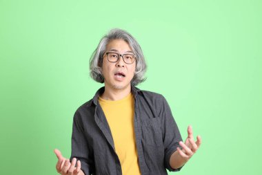 Kıdemli Asyalı, şık giyinmiş açık yeşil arka planda duruyor..