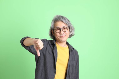 Kıdemli Asyalı, şık giyinmiş açık yeşil arka planda duruyor..