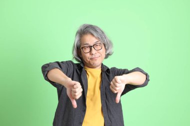 Kıdemli Asyalı, şık giyinmiş açık yeşil arka planda duruyor..