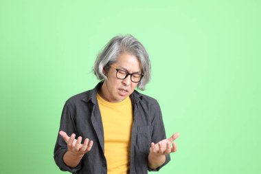 Kıdemli Asyalı, şık giyinmiş açık yeşil arka planda duruyor..