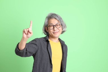 Kıdemli Asyalı, şık giyinmiş açık yeşil arka planda duruyor..