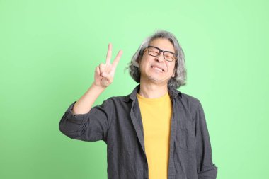 Kıdemli Asyalı, şık giyinmiş açık yeşil arka planda duruyor..