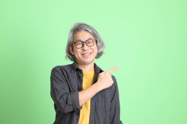 Kıdemli Asyalı, şık giyinmiş açık yeşil arka planda duruyor..