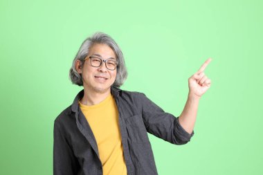 Kıdemli Asyalı, şık giyinmiş açık yeşil arka planda duruyor..
