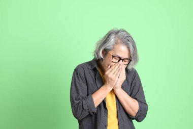 Kıdemli Asyalı, şık giyinmiş açık yeşil arka planda duruyor..