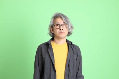 Kıdemli Asyalı, şık giyinmiş açık yeşil arka planda duruyor..