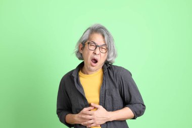 Kıdemli Asyalı, şık giyinmiş açık yeşil arka planda duruyor..