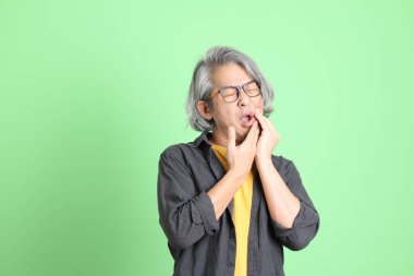 Kıdemli Asyalı, şık giyinmiş açık yeşil arka planda duruyor..