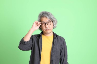 Kıdemli Asyalı, şık giyinmiş açık yeşil arka planda duruyor..
