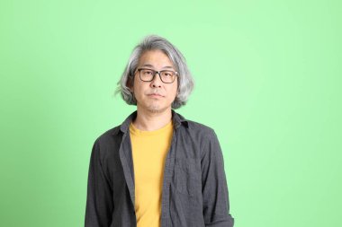 Kıdemli Asyalı, şık giyinmiş açık yeşil arka planda duruyor..