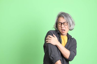 Kıdemli Asyalı, şık giyinmiş açık yeşil arka planda duruyor..