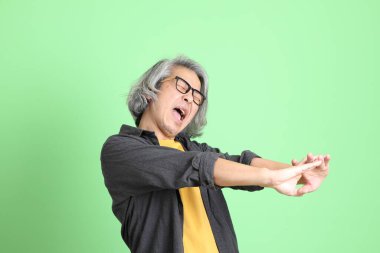 Kıdemli Asyalı, şık giyinmiş açık yeşil arka planda duruyor..