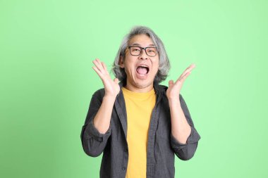 Kıdemli Asyalı, şık giyinmiş açık yeşil arka planda duruyor..