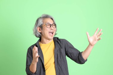 Kıdemli Asyalı, şık giyinmiş açık yeşil arka planda duruyor..