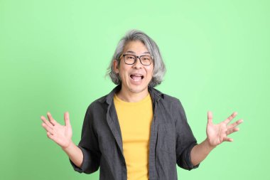 Kıdemli Asyalı, şık giyinmiş açık yeşil arka planda duruyor..