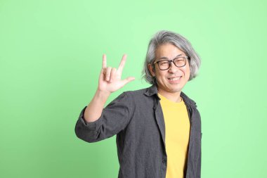 Kıdemli Asyalı, şık giyinmiş açık yeşil arka planda duruyor..