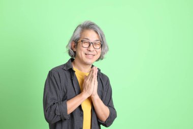 Kıdemli Asyalı, şık giyinmiş açık yeşil arka planda duruyor..