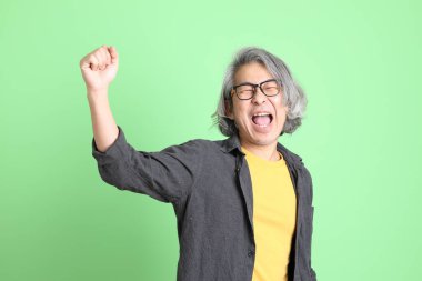 Kıdemli Asyalı, şık giyinmiş açık yeşil arka planda duruyor..