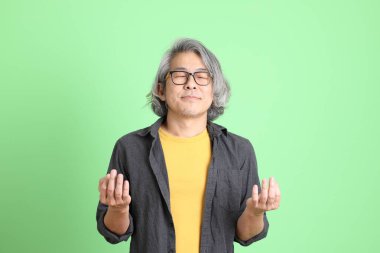 Kıdemli Asyalı, şık giyinmiş açık yeşil arka planda duruyor..