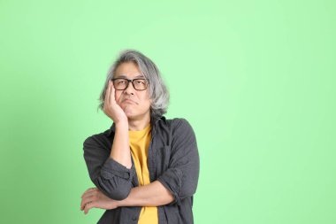 Kıdemli Asyalı, şık giyinmiş açık yeşil arka planda duruyor..