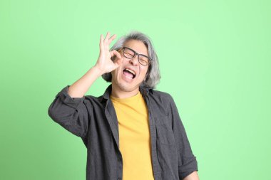 Kıdemli Asyalı, şık giyinmiş açık yeşil arka planda duruyor..