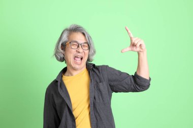 Kıdemli Asyalı, şık giyinmiş açık yeşil arka planda duruyor..