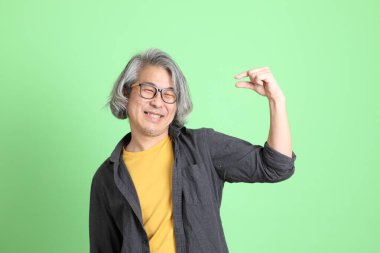 Kıdemli Asyalı, şık giyinmiş açık yeşil arka planda duruyor..