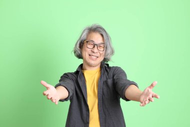 Kıdemli Asyalı, şık giyinmiş açık yeşil arka planda duruyor..