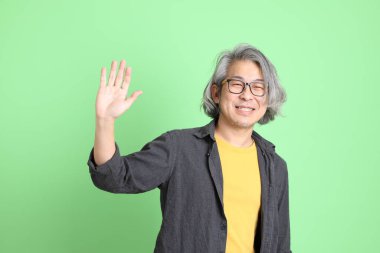 Kıdemli Asyalı, şık giyinmiş açık yeşil arka planda duruyor..