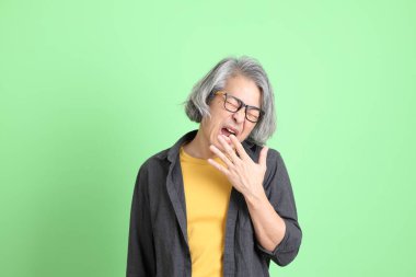 Kıdemli Asyalı, şık giyinmiş açık yeşil arka planda duruyor..