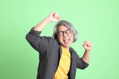 Kıdemli Asyalı, şık giyinmiş açık yeşil arka planda duruyor..