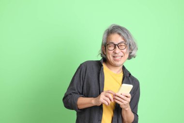 Kıdemli Asyalı, şık giyinmiş açık yeşil arka planda duruyor..