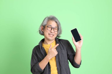 Kıdemli Asyalı, şık giyinmiş açık yeşil arka planda duruyor..