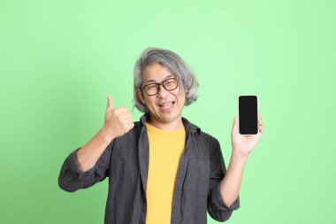 Kıdemli Asyalı, şık giyinmiş açık yeşil arka planda duruyor..