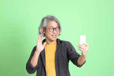 Kıdemli Asyalı, şık giyinmiş açık yeşil arka planda duruyor..