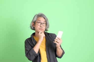 Kıdemli Asyalı, şık giyinmiş açık yeşil arka planda duruyor..