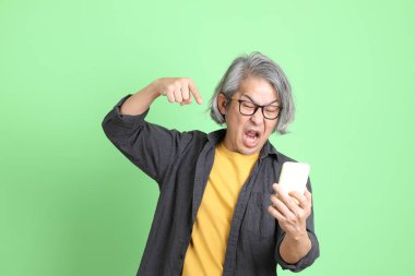 Kıdemli Asyalı, şık giyinmiş açık yeşil arka planda duruyor..