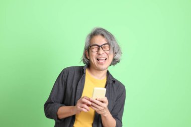 Kıdemli Asyalı, şık giyinmiş açık yeşil arka planda duruyor..