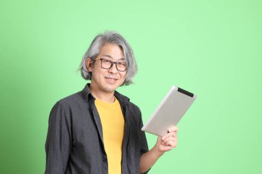 Kıdemli Asyalı, şık giyinmiş açık yeşil arka planda duruyor..