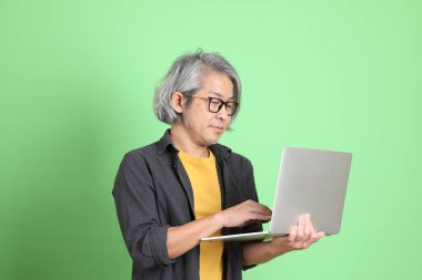 Kıdemli Asyalı, şık giyinmiş açık yeşil arka planda duruyor..