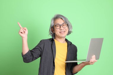 Kıdemli Asyalı, şık giyinmiş açık yeşil arka planda duruyor..