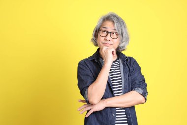 Sarı arka planda kot giymiş kıdemli Asyalı adam..